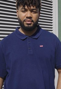 Marineblauwe polo in katoenmateriaal, met een kraag, drie knopen en een klein rood Levi's-logo op de borst.