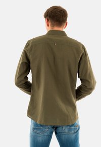 Olijfgroene langemouwen shirt met een kraag, rugpaneel detail en klein logo. Getoond in combinatie met lichtblauwe spijkerbroek.