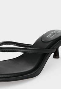 Μαύρο δερμάτινο σανδάλι με τακούνι, λεπτά διπλά λουράκια και κοντό, καμπυλωτό τακούνι kitten σε ανοιχτό φόντο.