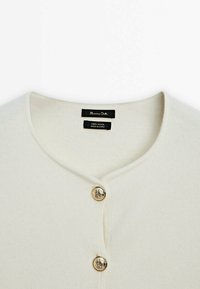 Cream-colored wool cardigan featuring a v-neckline, three round gold buttons, and a smooth textured fabric. Tags for wool and brand included.