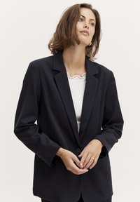 Dark navy blazer with a notched lapel, single button closure, and long sleeves. Features subtle stitching detail and relaxed fit.