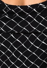 Svart tyg med ett rutmönster i vitt. Materialet verkar slätt med en lätt lyster och är draperat mjukt, vilket skapar veck.