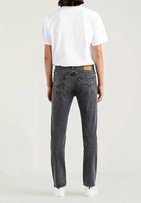 Vaqueros de mezclilla gris con un corte recto clásico, que cuentan con bolsillos traseros, una textura desgastada y una etiqueta de cuero en la cintura. Combinados con una camiseta blanca.