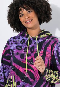 Sudadera colorida con una mezcla de patrones morados, negros y verde neón, con acentos texturizados y detalles decorativos.