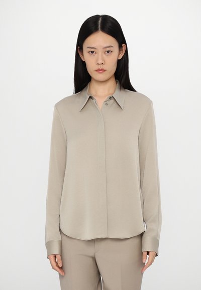 Blouse beige à manches longues en tissu lisse, avec un col et des détails de boutons, assortie à un pantalon beige.