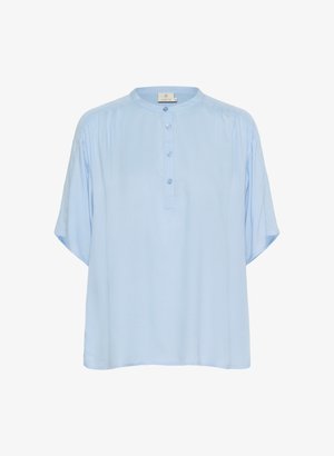 Blouse bleu clair à manches courtes avec un col rond, fermeture par boutons, plis aux épaules et une coupe ample et décontractée. Texture de tissu lisse.