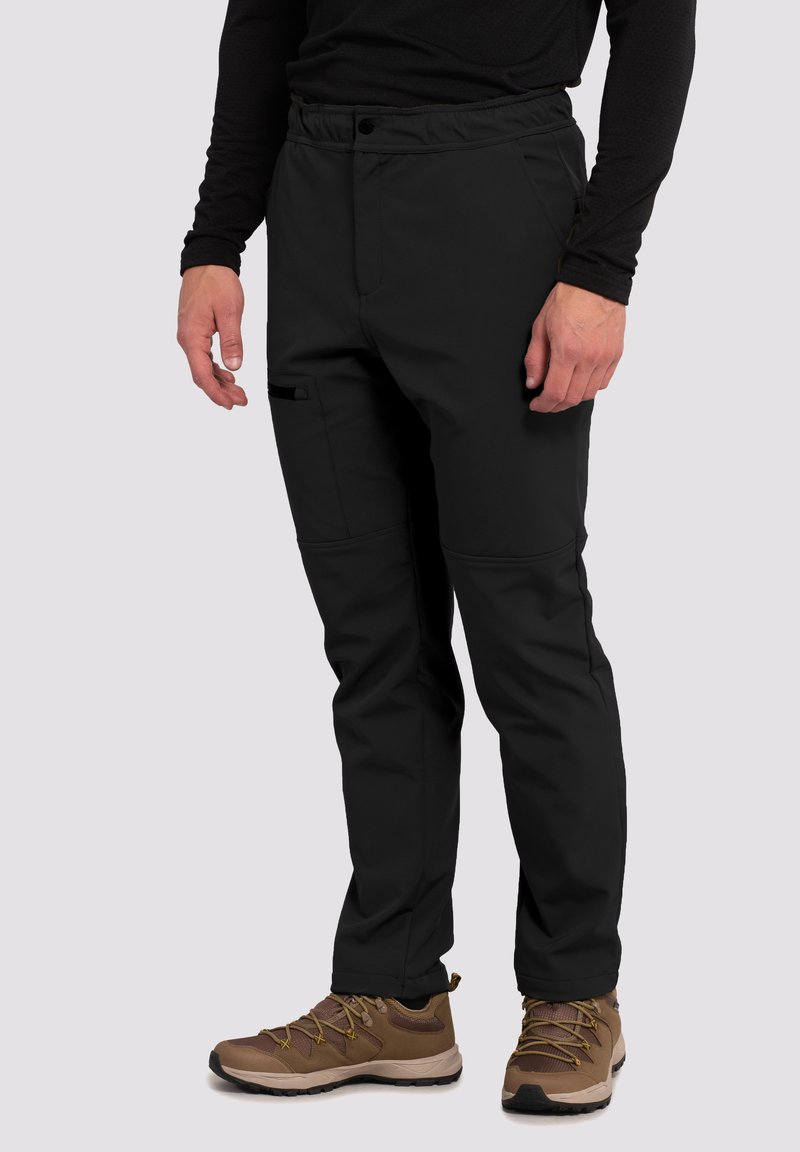 Sorte softshell-bukser har en afslappet pasform, elastisk linning, sidelommer og forstærkede knæ. De er parret med brune vandrestøvler.