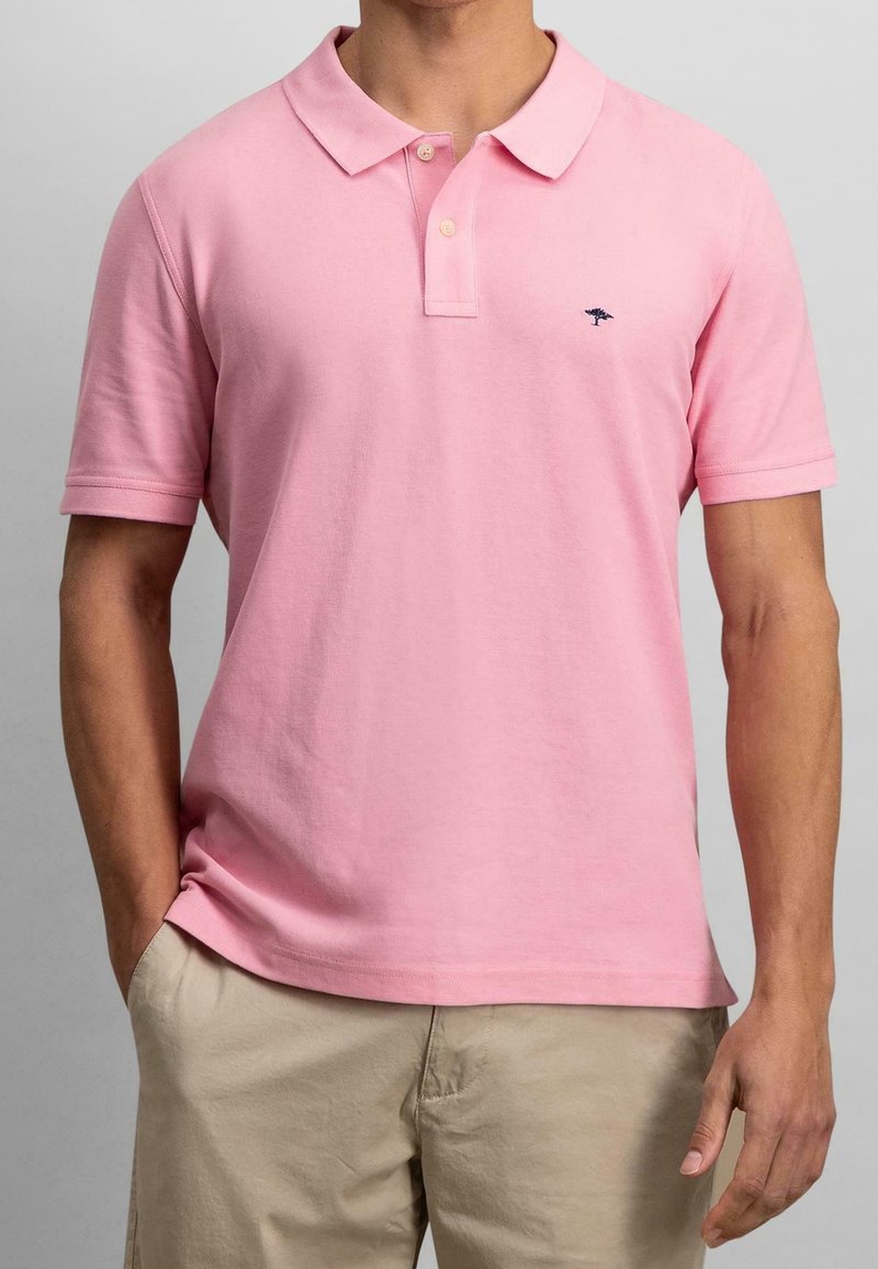 Polo rose clair en coton, avec un col classique, des manches courtes et un petit logo bleu marine sur la poitrine gauche.