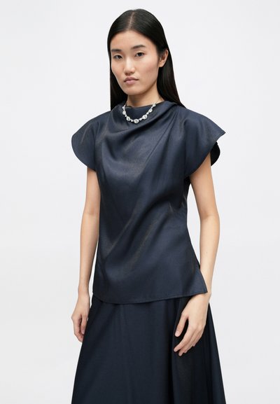 Navy blue short-sleeve top with a glossy texture, featuring wide, structured sleeves and a flowing silhouette. Paired with a matching skirt.