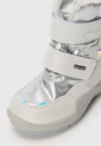 Bota metálica de plata con correas de velcro, cuello de piel sintética y suela texturizada gris. Presenta una membrana impermeable y acentos coloridos.