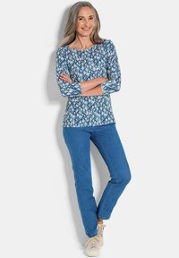 Maglietta a maniche lunghe con un motivo geometrico blu, abbinata a jeans blu e sneakers chiare. Vestibilità comoda con scollo rotondo.