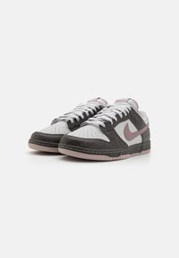 Low-top sneakers featuring white and gray leather, textured black overlays, a pink swoosh, and white laces with a pink outsole.