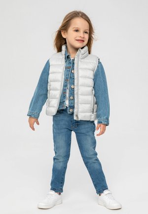 Ljust grått puffy väst över en blå denimskjorta med knappar, matchat med blå jeans och vita sneakers. Slät, glänsande textur.