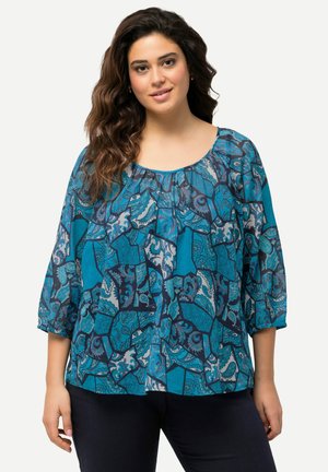 Blusa blu con pattern a maniche tre quarti, in tessuto testurizzato che presenta un mix di motivi paisley e forme astratte in diverse tonalità di blu.