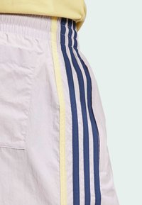 Helle Shorts mit Seitentaschen, die navyblaue und gelbe vertikale Streifen aufweisen. Glatte Textur und elastischer Bund.