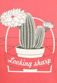 Kaktusillustration i grå i en hvid potte, dekoreret med blomster, på en koralbaggrund. Inkluderer teksten "Looking sharp" på en hvid banner.