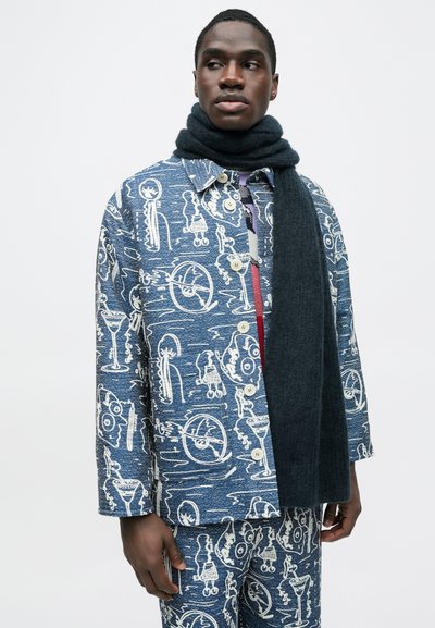 Μπλε μπουφάν με σχέδια σε λευκό, με κουμπιά μπροστά, σετ με ταιριαστό παντελόνι και σκοτεινό κασκόλ. Το ύφασμα φαίνεται υφασμένο και με υφή.