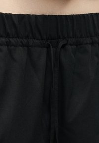 Ελαστική ζώνη μέσης με μαύρο κορδόνι από ύφασμα σε μαύρο παντελόνι, κοντινή λήψη που δείχνει υφή υφάσματος και βελονιές που συγκεντρώνονται.