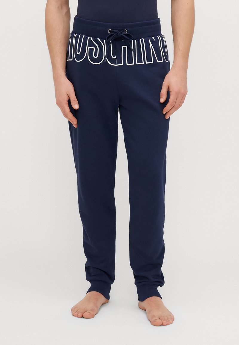 Tmavomodré tepláky s elastickým pásom a šnúrkou, s veľkým bielym logom "Moschino" pozdĺž pásu a s manžetami na členkoch.