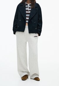 Granatowy dwurzędowy płaszcz typu peacoat, paskowany krótki top, szare szerokie dresy z logo "santa monica" oraz brązowe zamszowe buty wsuwane.