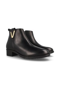 Botas de tobillo de cuero negro con un tacón de bloque bajo, punta redondeada y una "V" dorada decorativa en la parte trasera. Textura suave, diseño minimalista.