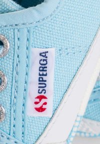 Sneaker in tela azzurra chiara con suola in gomma bianca, occhielli in argento e un'etichetta con il logo "Superga" nei colori rosso e blu.