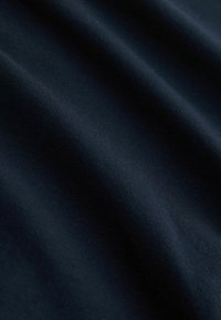 Gros plan sur un tissu bleu foncé à texture côtelée fine avec des plis doux créant des ombres subtiles.