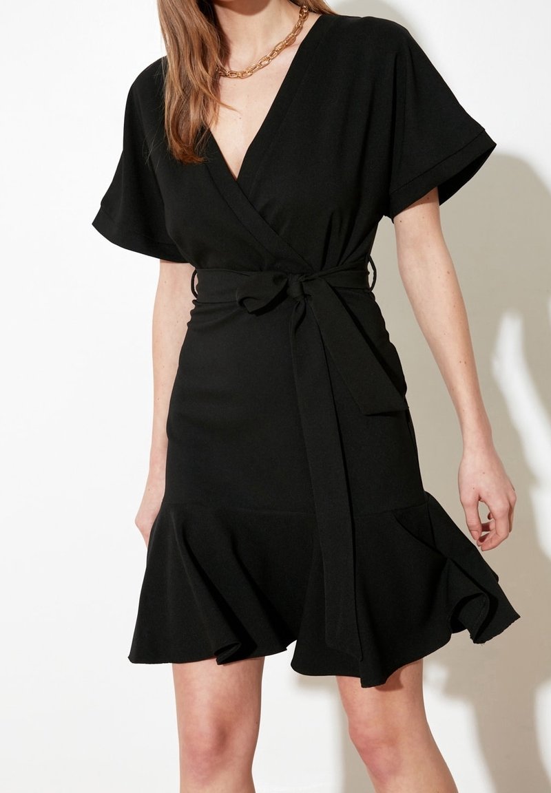 Robe noire à manches courtes larges, avec une taille cintrée et un ourlet à volants. Fabriquée en tissu lisse, avec un décolleté en V profond.