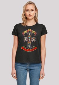Black cotton t-shirt featuring a graphic design of a cross with skulls and the text "Guns N' Roses" and "Appetite for Destruction" in red.