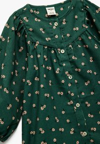 Vestido verde abotonado con una tela texturada, con un patrón floral en rosa claro. Mangas abullonadas y detalle de cintura fruncida.