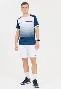 Blå och vit idrottströja med gradierad design, kombinerad med vita shorts. Svarta skor med grå detaljer och vita strumpor. Minimal varumärkesprofil.