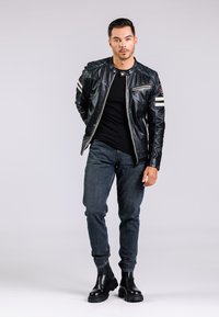 Chaqueta de motocicleta de cuero negro con franjas plateadas, camiseta negra ajustada, vaqueros azul oscuro y botas negras de tobillo con suelas gruesas.