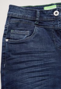 Jeans de mezclilla azul oscuro con una textura ligeramente desgastada, que cuentan con un bolsillo frontal, cierre de botón y costuras de acento verdes en la cintura.