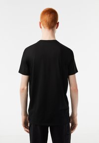 Camiseta de manga corta negra hecha de algodón; presenta un cuello redondo y un diseño trasero limpio y sencillo sin ninguna decoración.