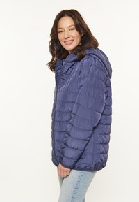Chaqueta acolchada navy con capucha, que presenta secciones acolchadas horizontales, un zipper de longitud completa y una textura suave y brillante.