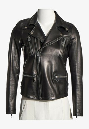 Chaqueta de cuero negra con cremallera asimétrica, cuatro bolsillos con cremallera y detalles metálicos en el cuello con botones a presión en un torso de maniquí blanco.