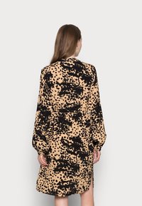 Långärmad klänning i beige med svart djurtryck, försedd med ett bälte i midjan och sidöppningar, tillverkad av mjuk, lättviktsmaterial.