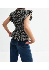 Top peplum nero con fiori, maniche arricciate, vita smoccolata e dettaglio a oblò sul retro, abbinato a jeans in denim blu a vita alta.
