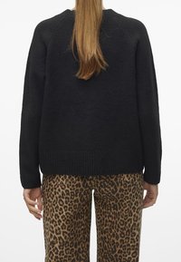 Pull noir en maille avec ourlet côtelé et manches raglan, associé à un pantalon imprimé léopard. Tissu texturé visible sur le pull.
