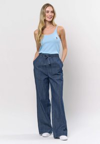 Top albastru deschis cu dungi, cu decolteu rotund și logo mic, asortat cu pantaloni largi din denim închis la culoare, cu talie elastică și șnur reglabil.