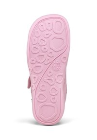 Semelle en caoutchouc rose d'une chaussure d'enfant avec des motifs géométriques texturés et un petit visage souriant près du centre.