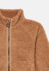 Καφέ ζακέτα από φλις με ψηλό γιακά, διαθέτει ολόκληρο φερμουάρ και υφή με βρόχους. Ελαφριά με μανίκια ραγκλάν.