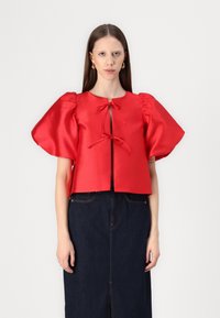 Cropped top in satiny rosso con maniche a sbuffo e chiusura con nodo frontale, abbinato a una gonna in denim scuro; texture liscia e colore vibrante.