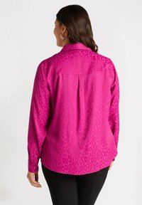 Fuchsia-blus med leopardmönster, knäppte manschetter, krage och rundad nederkant, tillverkad av ett mjukt, lätt tyg.