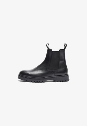 Botas Chelsea pretas em couro com acabamento texturizado, painéis laterais elásticos e alças de puxar. Apresentam uma sola de borracha robusta com ranhuras.