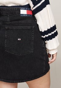 Jupe en denim noir au design ajusté, dotée d'une poche arrière avec une étiquette logo colorée et de détails de couture subtils.