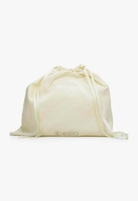 Bavlněný drawstring pytel v krémové barvě s hladkým povrchem. Obsahuje stažený vršek se stužkovými úvazy a jemně embosované logo na přední straně.