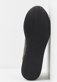 Semelle d'une basket foncée avec un motif de bande de roulement ondulé, taille marquée 37, photographiée sur fond blanc.