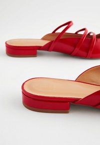 Sandales à talons rouges avec des fines brides croisées, une finition brillante et un talon bloc. La semelle est beige avec un détail de marque en relief.