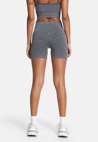 Sivý športový top a zodpovedajúce vysoko pásové šortky, vyrobené z textúrovaného, elastického materiálu. Nosené s bielymi ponožkami a svetlými športovými topánkami.